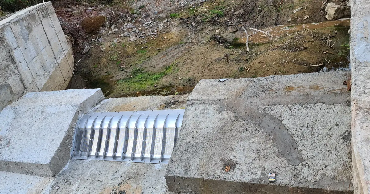 A Coanda intake screen set into a concrete weir in a rocky streambed