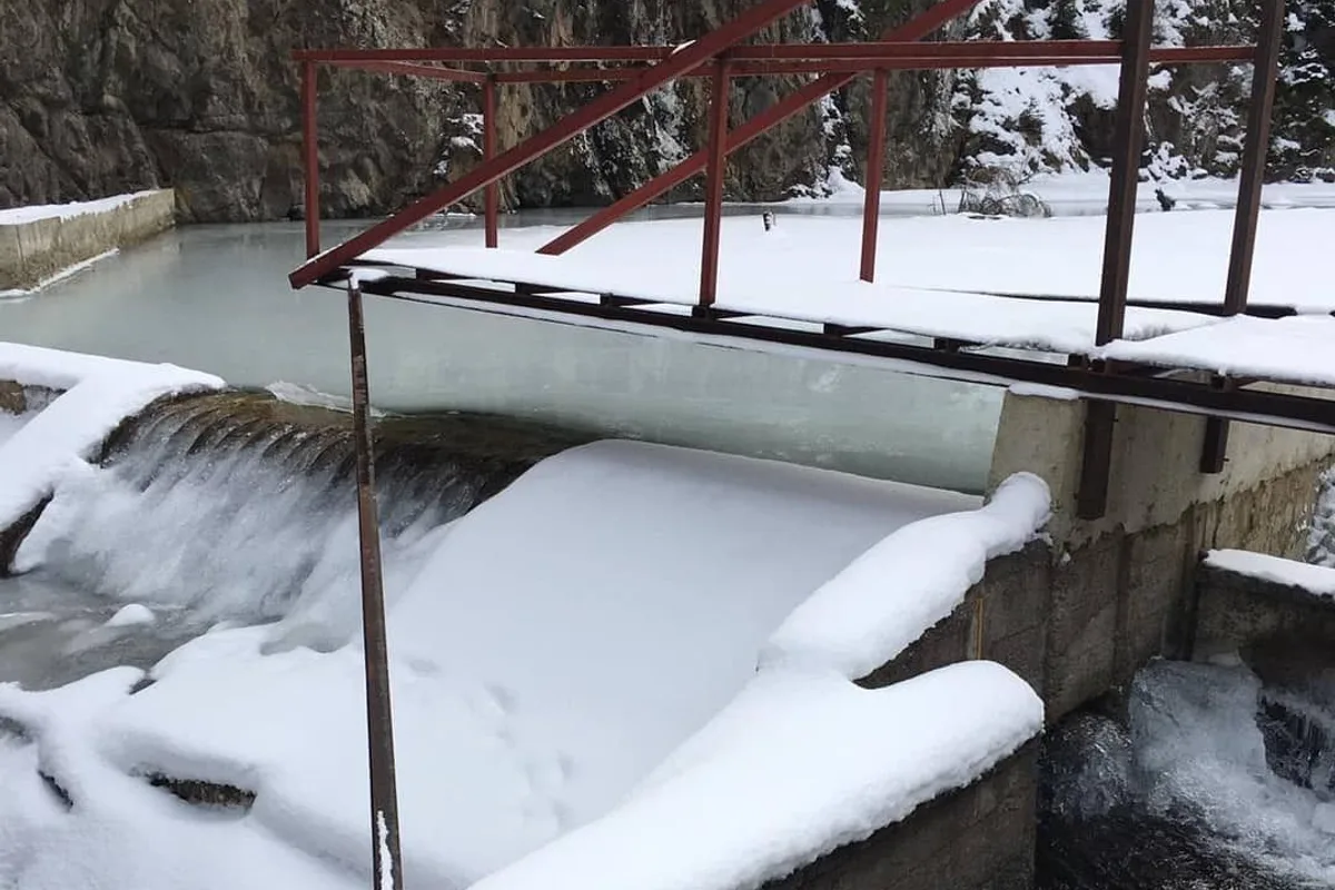 A snow-covered concrete weir with a Coanda intake screen along its crest, water running over the screen face