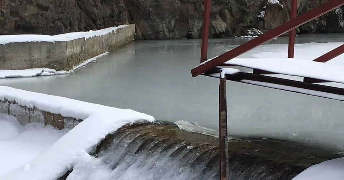 A Coanda intake screen working in winter, snow lying deep on the weir and the surrounding structure while water sheets across the screen face