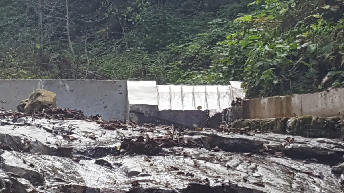 A stream bed filled with boulders and flood-borne surface debris beside a concrete intake structure