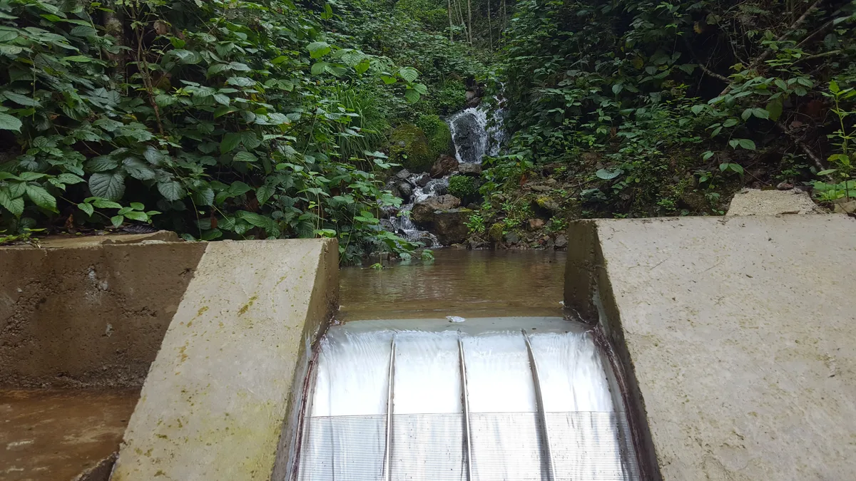 A Coanda intake screen in operation on a concrete weir, water sheeting across the full width of the screen face