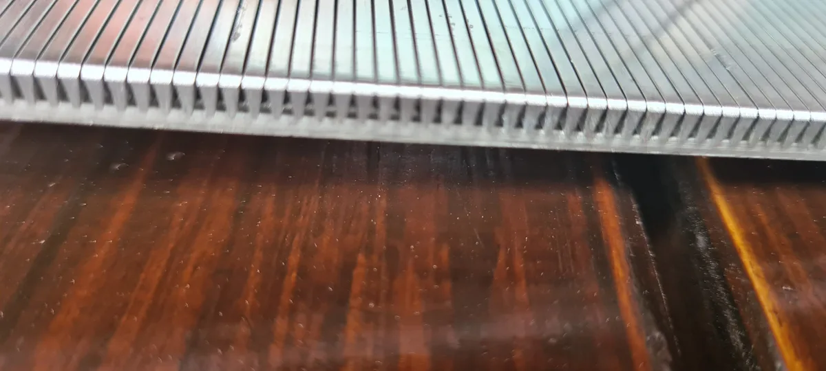 A section of a Coanda intake screen resting on a workshop bench, slots seen along its surface