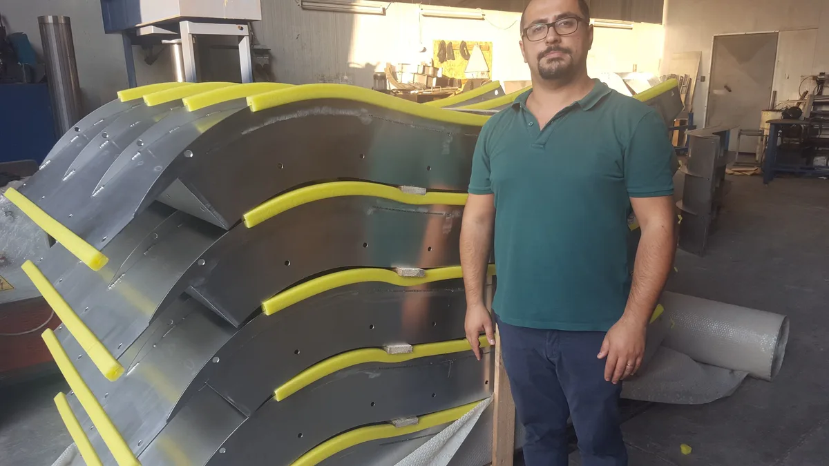A worker standing beside a stack of finished Coanda screen bodies in the workshop