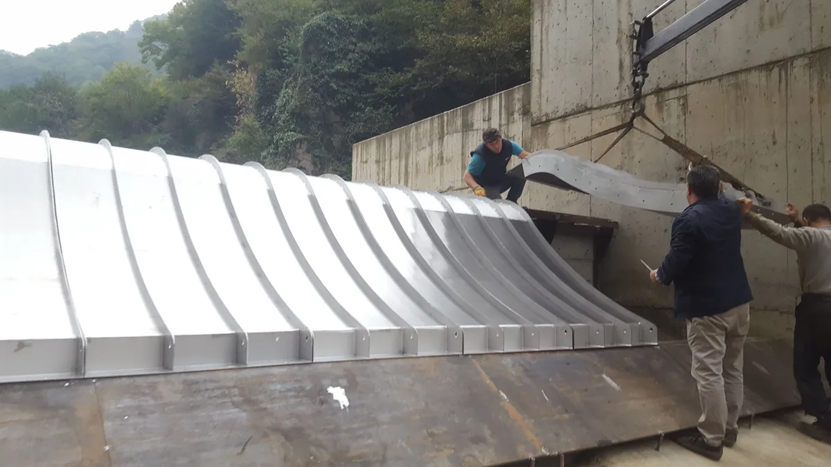 Ein großer Coanda-Rechenkörper wird in einem Einlaufbauwerk aus Beton eingesetzt, Arbeiter daneben