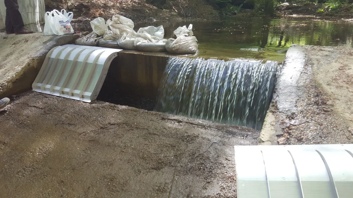 Ein kleiner Coanda-Einlaufrechen in einem Betonwehr, über das Wasser strömt
