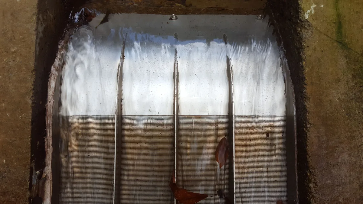 Una rejilla de toma Coanda en funcionamiento sobre un azud de hormigón, con el agua extendiéndose en lámina por todo el ancho de la cara de la rejilla