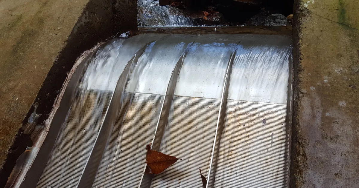 A Coanda intake screen in operation on a concrete weir, water sheeting across the full width of the screen face