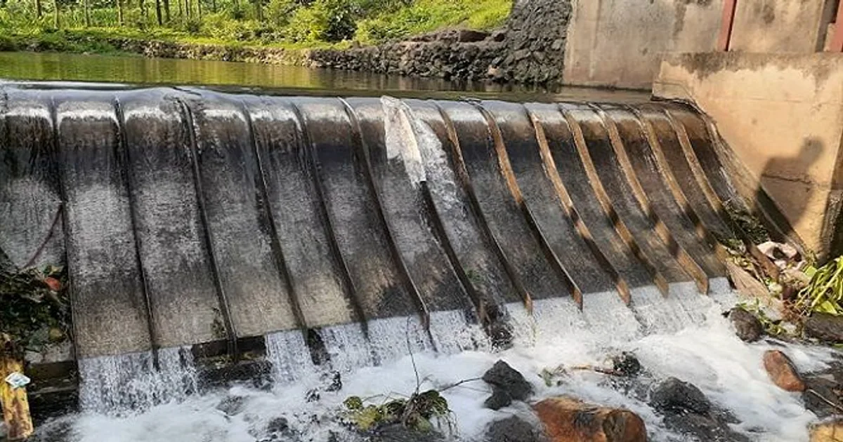 A Coanda intake screen set into a concrete weir across a rocky stream in Rwanda, water breaking over the screen face