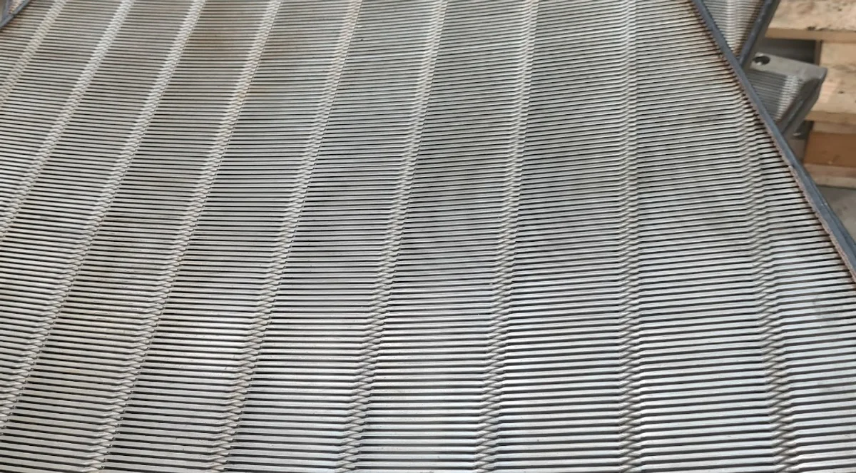 Close view of a curved wedge-wire panel in the workshop, the wires running across it and welded to the support bars beneath them