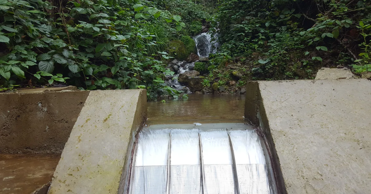 A Coanda intake screen in operation on a concrete weir, water sheeting across the full width of the screen face