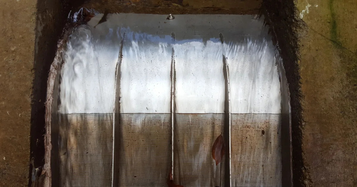 A Coanda intake screen in operation on a concrete weir, water sheeting across the full width of the screen face