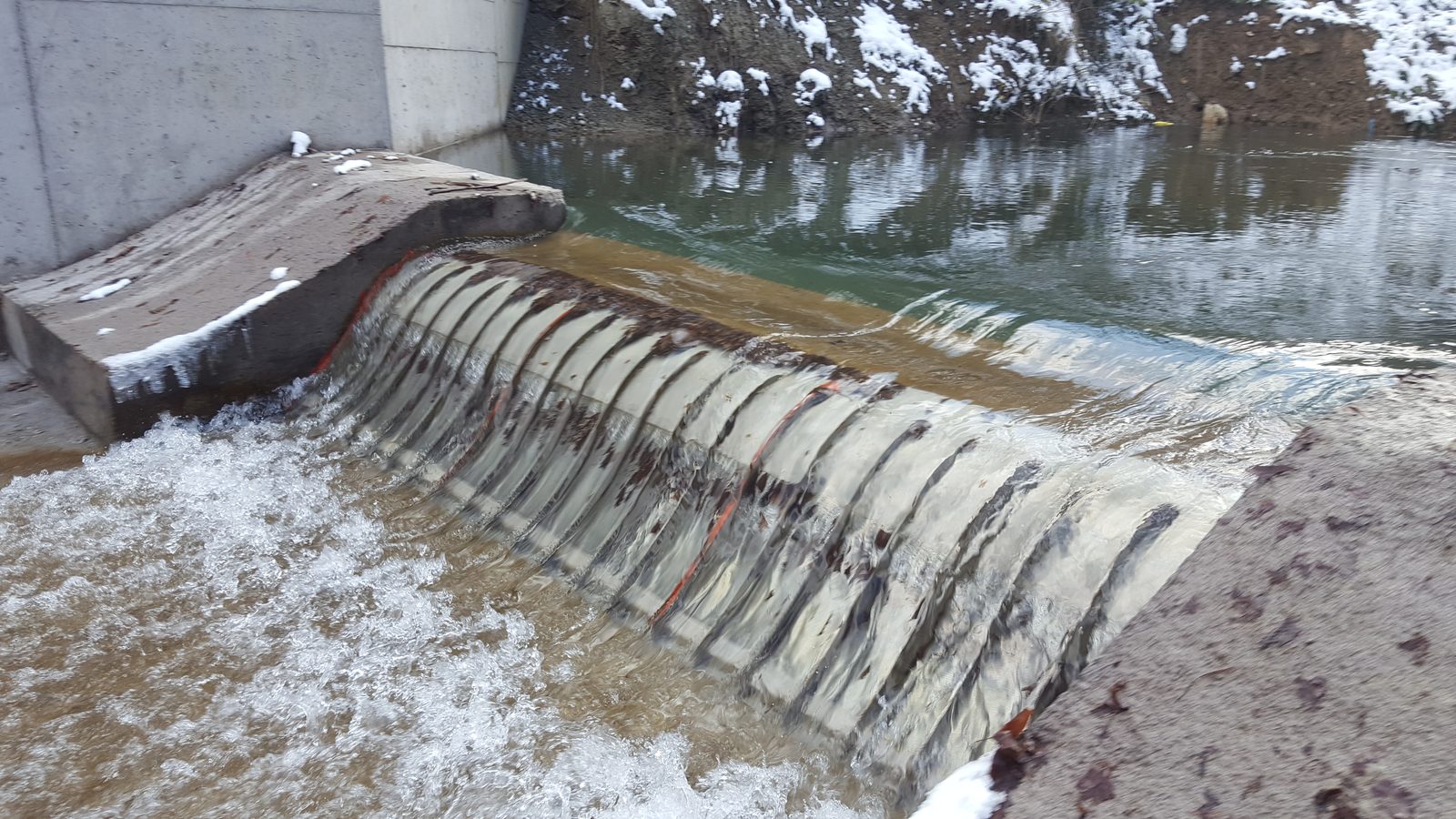 The Muratbey intake in January 2018, two months after commissioning: clear water pooled behind the weir and flowing in a thin sheet over three Coanda screens fitted with protection bars