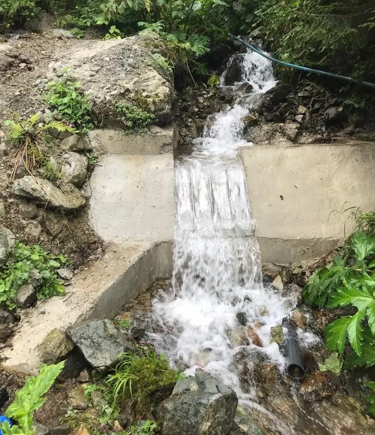 Derselbe Bach nach der Nachrüstung, das Wasser fließt in einem dünnen Film über einen ADENCO Coanda-Rechen, der in ein neues Betonwehr eingebaut ist
