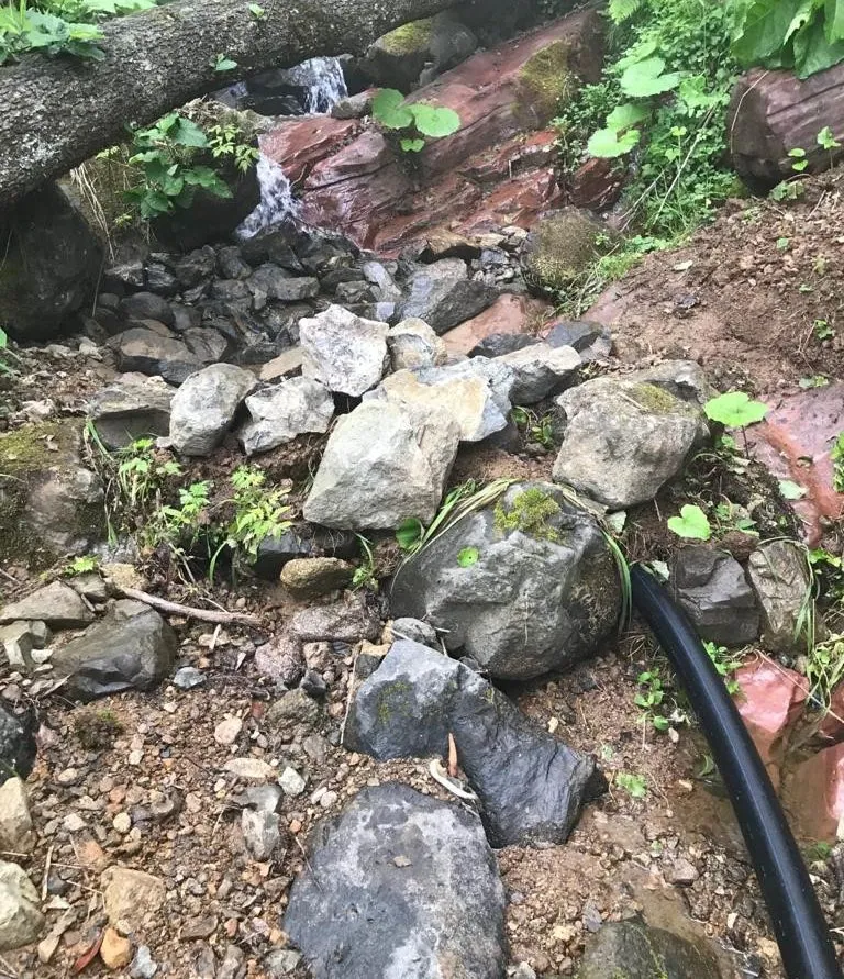 Çaykara, Wasserfassung Uzungöl vor der Nachrüstung: ein Kanal aus losem Gestein mit einem schwarzen Versorgungsrohr auf der Bachsohle