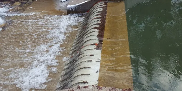 Rejillas de toma Coanda 3 x ADENCO-45-1, toma de 105 l/s para riego, rejilla Coanda larga sobre la cresta del azud con agua turbia que fluye en lámina fina sobre ella y agua embalsada detrás del azud, Bursa, Türkiye